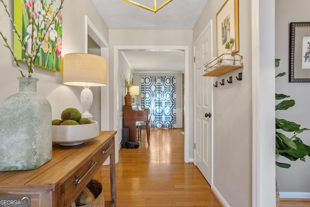 corridor featuring light wood finished floors, baseboards, and a textured ceiling