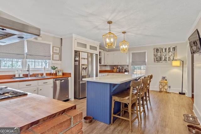 kitchen featuring white cabinets, stainless steel appliances, light countertops, pendant lighting, and a sink