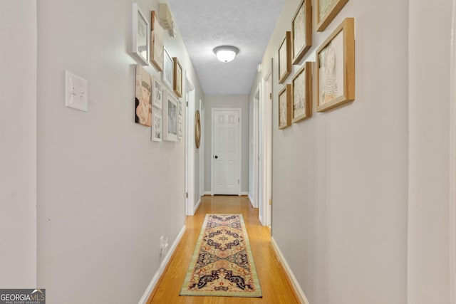 hallway featuring a textured ceiling, wood finished floors, and baseboards