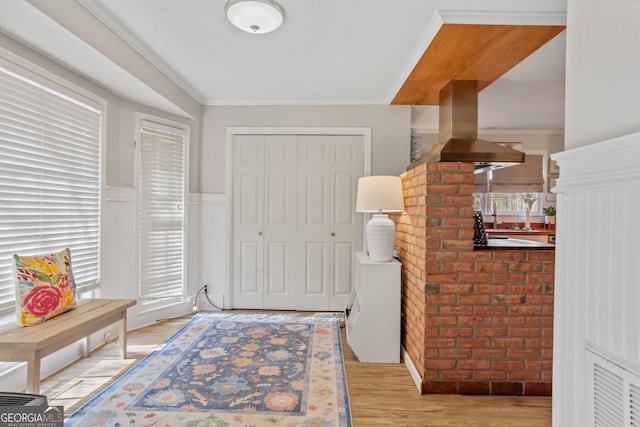 foyer featuring light wood-type flooring, a wainscoted wall, visible vents, and ornamental molding