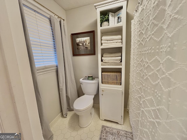 bathroom featuring toilet, tile patterned flooring, baseboards, and a textured ceiling