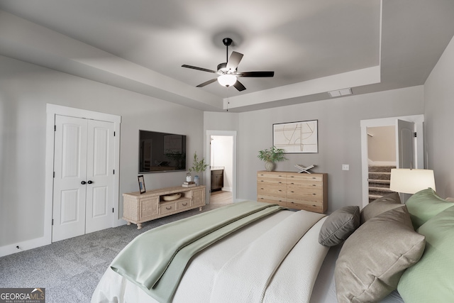 carpeted bedroom with a closet, ensuite bath, a raised ceiling, and ceiling fan