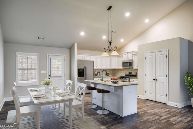 kitchen with a breakfast bar, white cabinetry, hanging light fixtures, stainless steel appliances, and a center island with sink