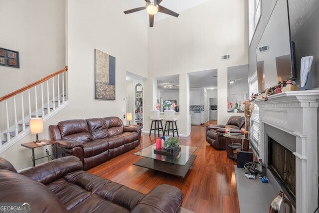 living room featuring dark wood-type flooring, ceiling fan, and a towering ceiling