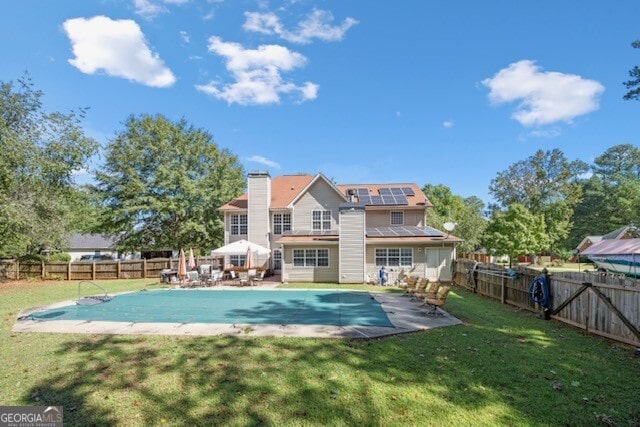 rear view of house with a patio, a covered pool, a lawn, and solar panels