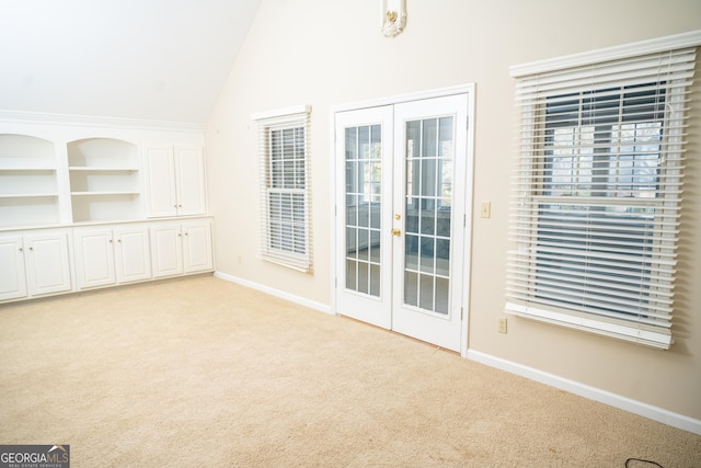 interior space with built in features, vaulted ceiling, light colored carpet, and french doors