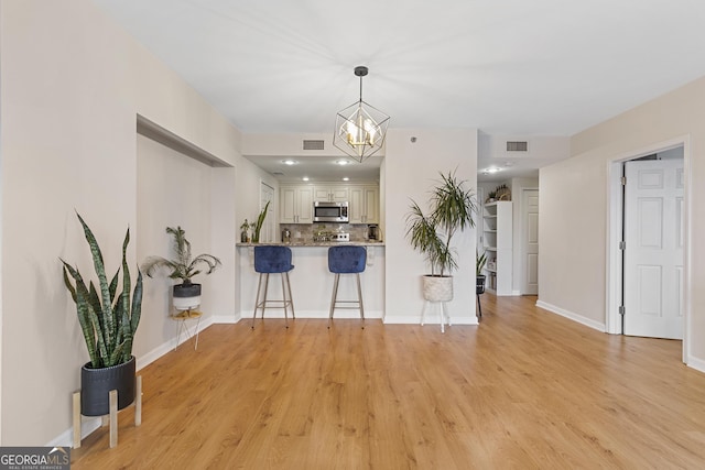 kitchen with light hardwood / wood-style flooring, a breakfast bar, backsplash, decorative light fixtures, and kitchen peninsula