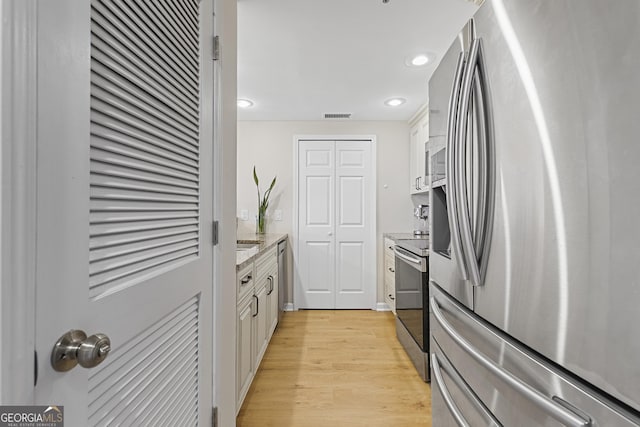 kitchen with stainless steel appliances, white cabinetry, and light hardwood / wood-style floors