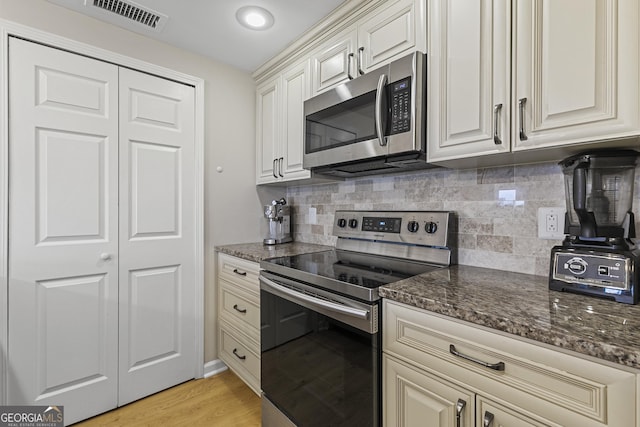 kitchen with stainless steel appliances, light hardwood / wood-style floors, decorative backsplash, and dark stone counters