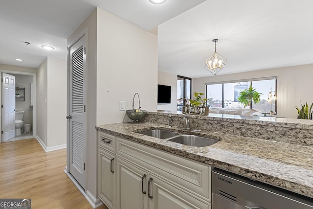 kitchen with sink, a chandelier, stainless steel dishwasher, light stone counters, and light hardwood / wood-style flooring