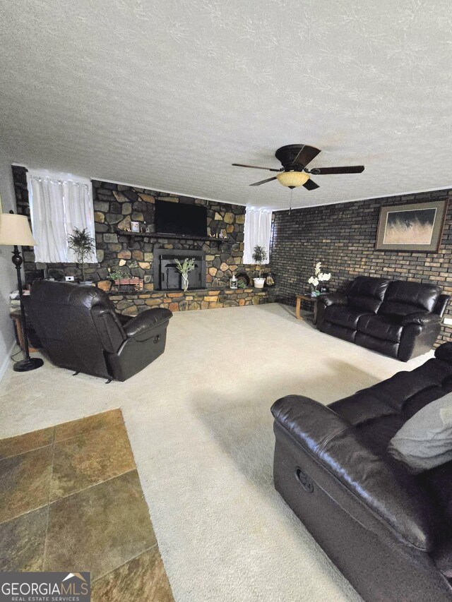 living room featuring ceiling fan, a stone fireplace, and a textured ceiling