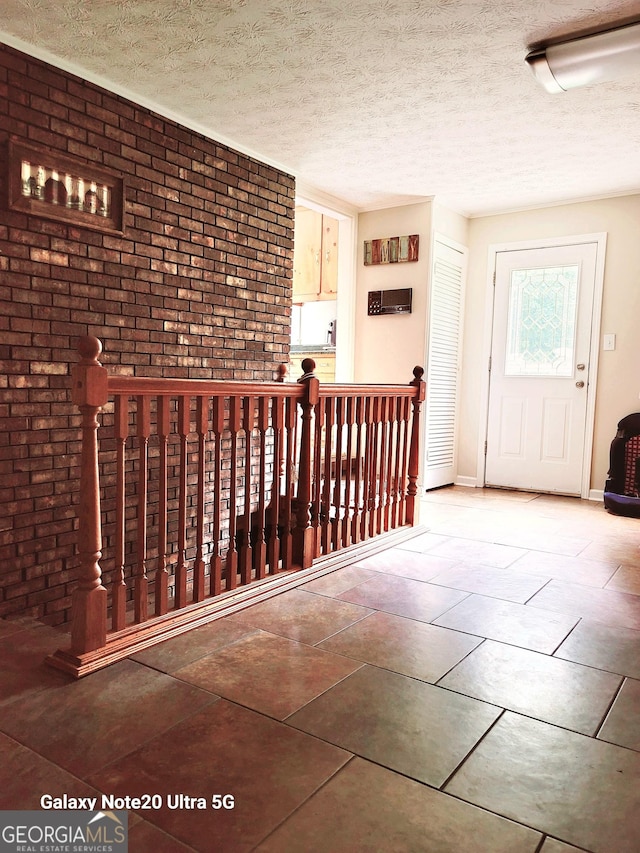 interior space with baseboards, brick wall, tile patterned flooring, a textured ceiling, and an upstairs landing