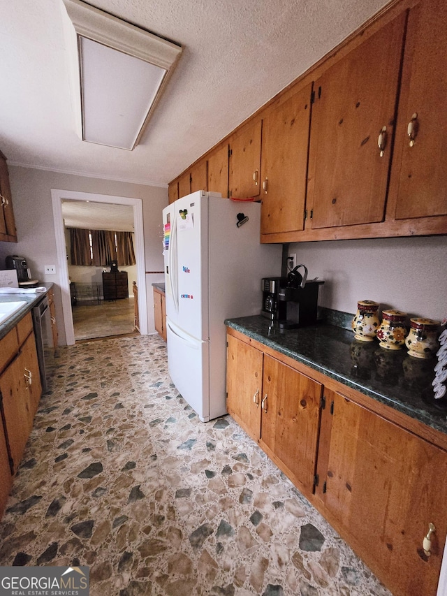 kitchen featuring stone finish floor, dark countertops, freestanding refrigerator, and brown cabinets