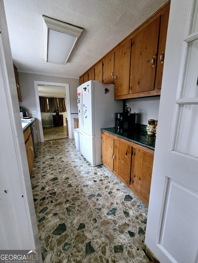 kitchen with dark countertops, brown cabinetry, freestanding refrigerator, stone finish flooring, and a textured ceiling