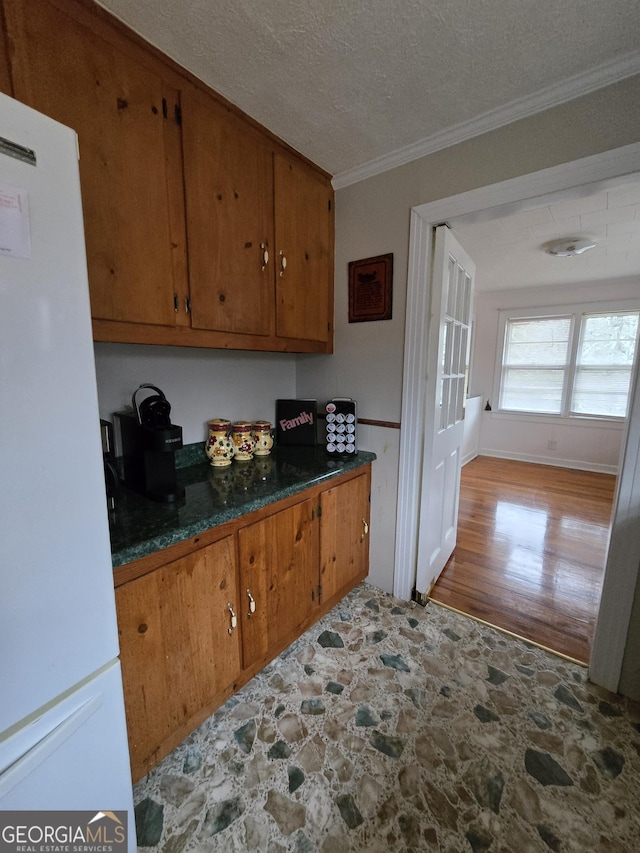 kitchen featuring a textured ceiling, ornamental molding, brown cabinetry, and freestanding refrigerator