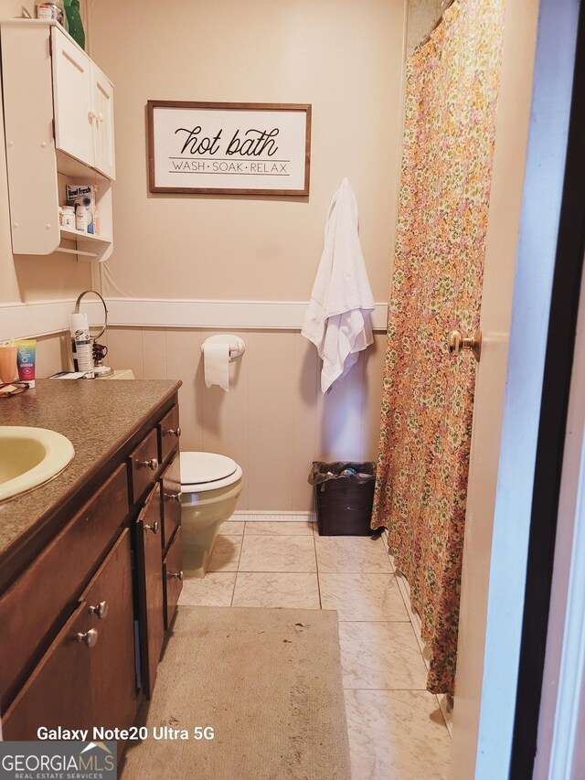 full bathroom with a wainscoted wall, a shower with shower curtain, toilet, vanity, and tile patterned flooring