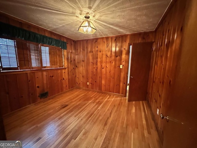 unfurnished room featuring hardwood / wood-style floors, a textured ceiling, and wood walls