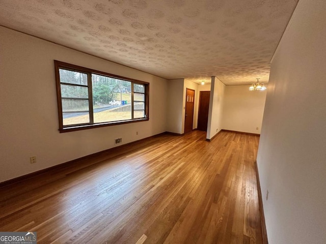 spare room featuring light wood-type flooring, a notable chandelier, and a textured ceiling