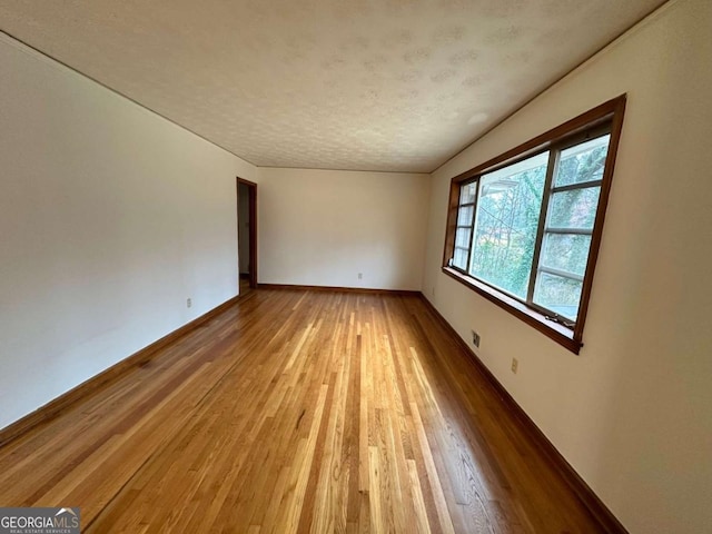 unfurnished room with a textured ceiling and light wood-type flooring