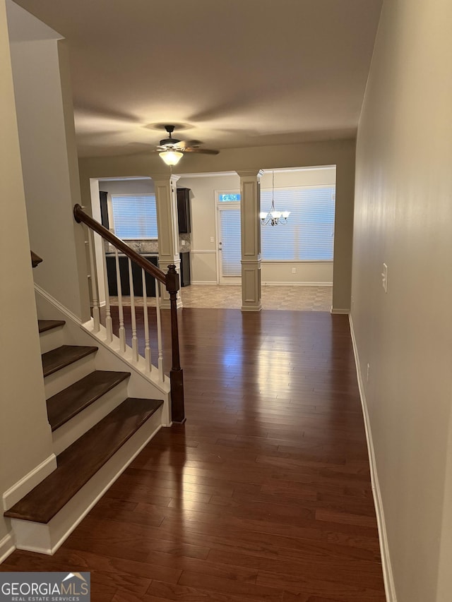 staircase featuring decorative columns, ceiling fan with notable chandelier, and hardwood / wood-style floors