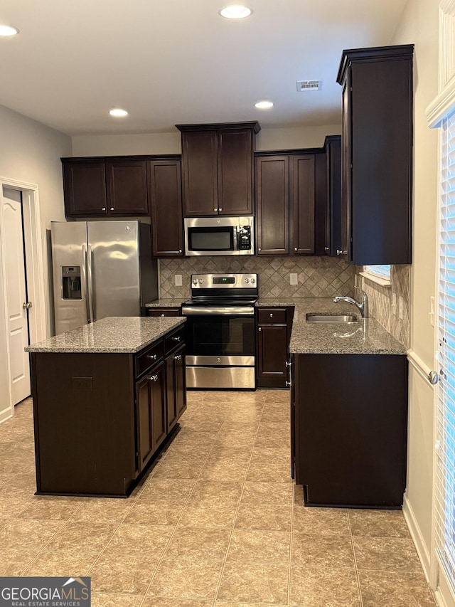 kitchen with dark brown cabinetry, sink, light stone counters, appliances with stainless steel finishes, and a kitchen island