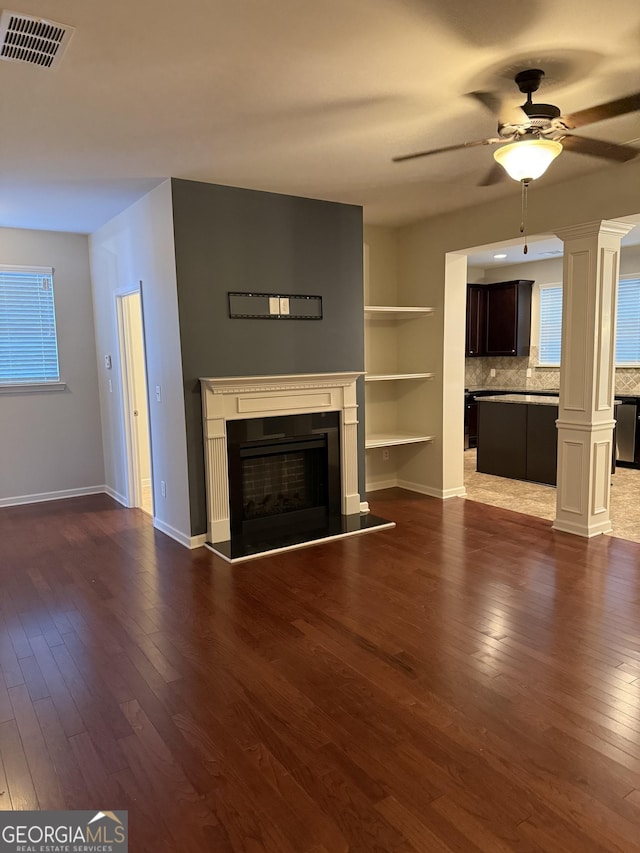 unfurnished living room featuring ornate columns, ceiling fan, and dark hardwood / wood-style flooring