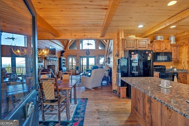 kitchen with beam ceiling, wooden walls, wood-type flooring, black appliances, and a stone fireplace