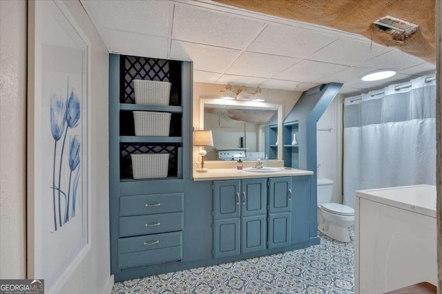 bathroom featuring a drop ceiling, vanity, built in shelves, and toilet