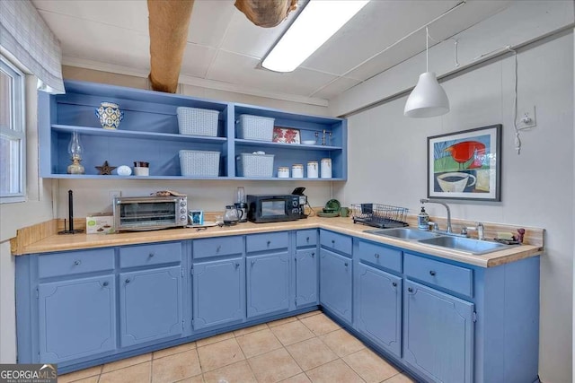 kitchen featuring blue cabinets, sink, light tile patterned floors, and decorative light fixtures