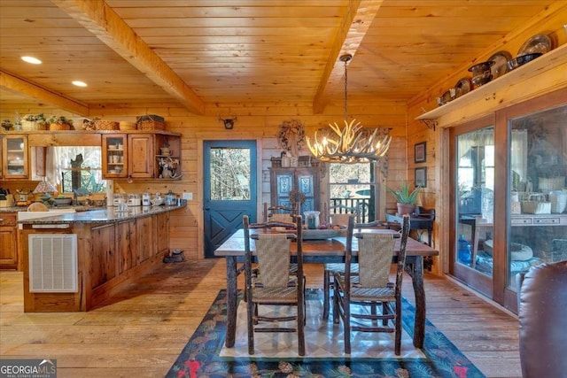 dining room featuring beamed ceiling, a healthy amount of sunlight, wooden walls, and light hardwood / wood-style flooring