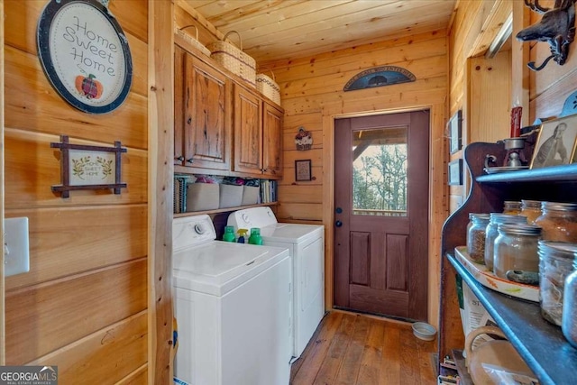 clothes washing area with wood walls, cabinets, wood ceiling, washing machine and dryer, and light wood-type flooring