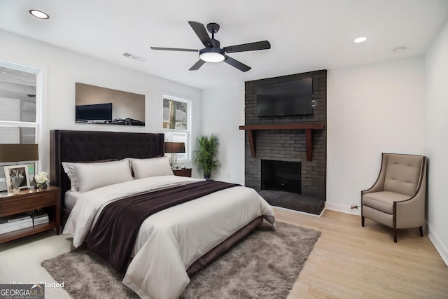 bedroom featuring ceiling fan, a brick fireplace, and light wood-type flooring