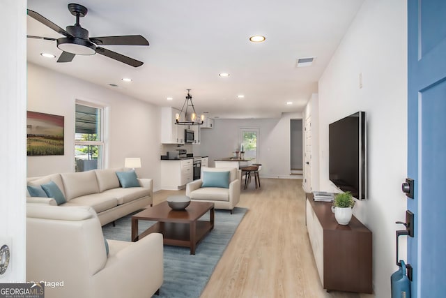 living room with plenty of natural light, ceiling fan with notable chandelier, and light wood-type flooring