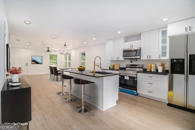 kitchen with sink, white cabinetry, stainless steel appliances, a center island with sink, and decorative backsplash