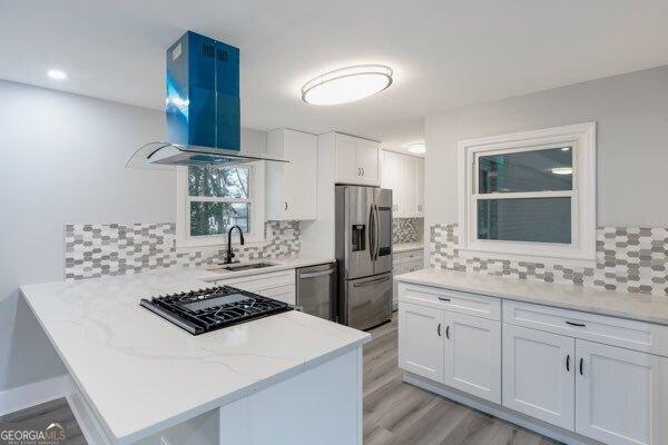 kitchen featuring white cabinetry, stainless steel appliances, kitchen peninsula, and island exhaust hood