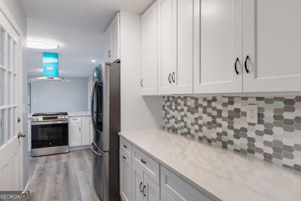 kitchen with appliances with stainless steel finishes, range hood, white cabinetry, decorative backsplash, and light hardwood / wood-style floors