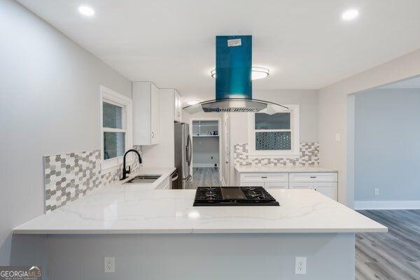 kitchen with sink, white cabinetry, kitchen peninsula, island exhaust hood, and black gas stovetop