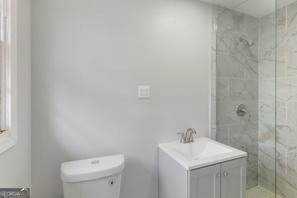 bathroom featuring vanity, toilet, and a tile shower