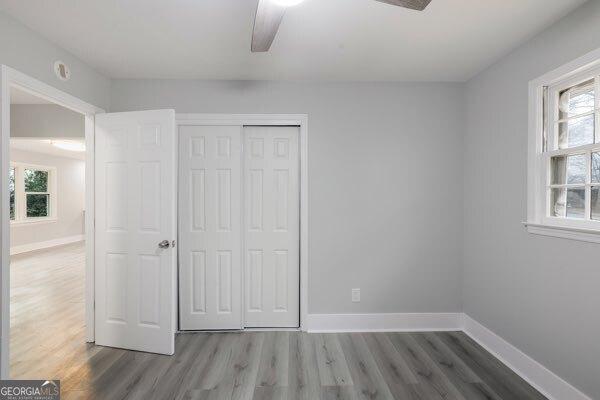 unfurnished bedroom featuring multiple windows, hardwood / wood-style floors, ceiling fan, and a closet