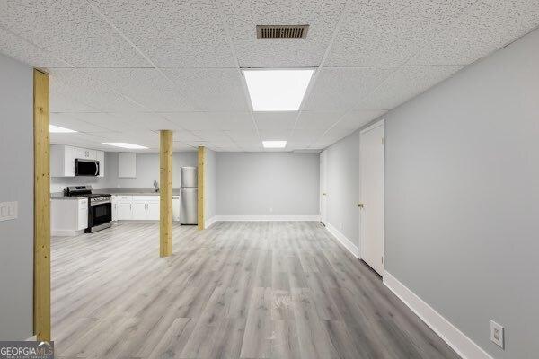 basement with a paneled ceiling, stainless steel fridge, and light wood-type flooring