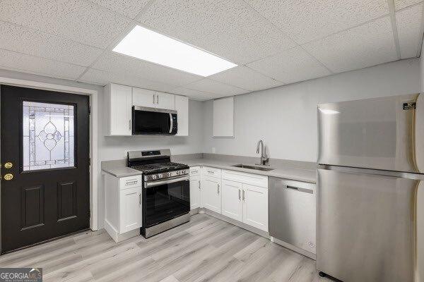 kitchen with a drop ceiling, stainless steel appliances, sink, and white cabinets