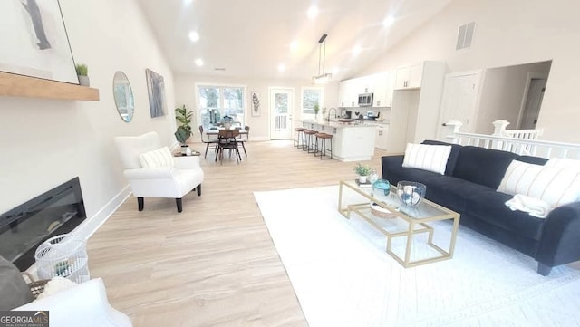 living room with sink, light hardwood / wood-style floors, and high vaulted ceiling