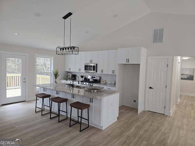 kitchen featuring stove, tasteful backsplash, light stone countertops, white cabinets, and a center island with sink