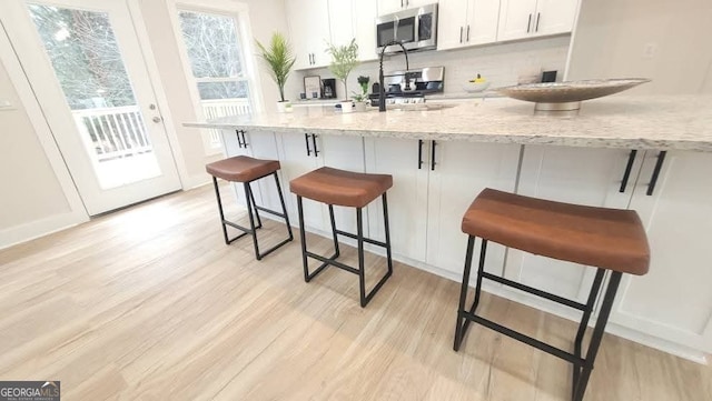 kitchen featuring light stone countertops, a breakfast bar, white cabinets, and light hardwood / wood-style flooring