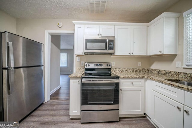 kitchen featuring light stone counters, hardwood / wood-style flooring, stainless steel appliances, and white cabinets