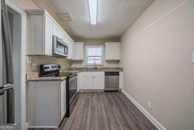 kitchen featuring appliances with stainless steel finishes, white cabinetry, sink, dark wood-type flooring, and a textured ceiling