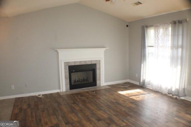 unfurnished living room featuring dark hardwood / wood-style floors, a tiled fireplace, and vaulted ceiling