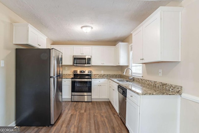 kitchen with dark hardwood / wood-style floors, white cabinetry, sink, light stone counters, and stainless steel appliances