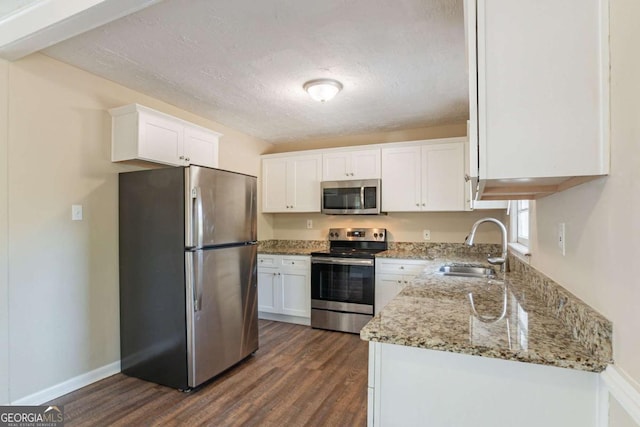 kitchen with sink, appliances with stainless steel finishes, white cabinetry, light stone countertops, and dark hardwood / wood-style flooring