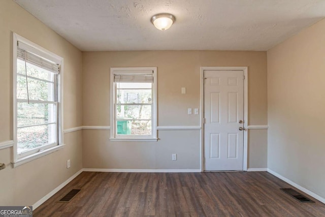 empty room with plenty of natural light, dark hardwood / wood-style floors, and a textured ceiling